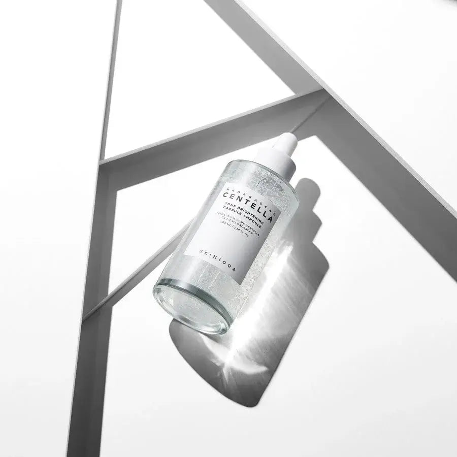 SKIN1004 Madagascar Tone Brightening Capsule Ampoule on a reflective surface, showcasing its hydrating formula.
